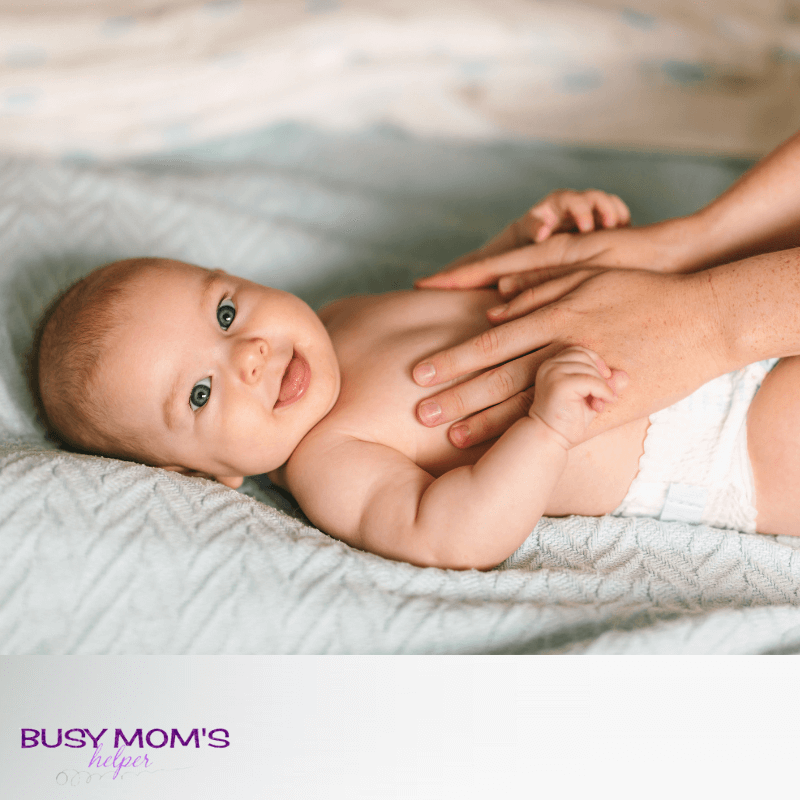 Photo of a baby on a blue blanket with a mother's hand touching it's stomach.